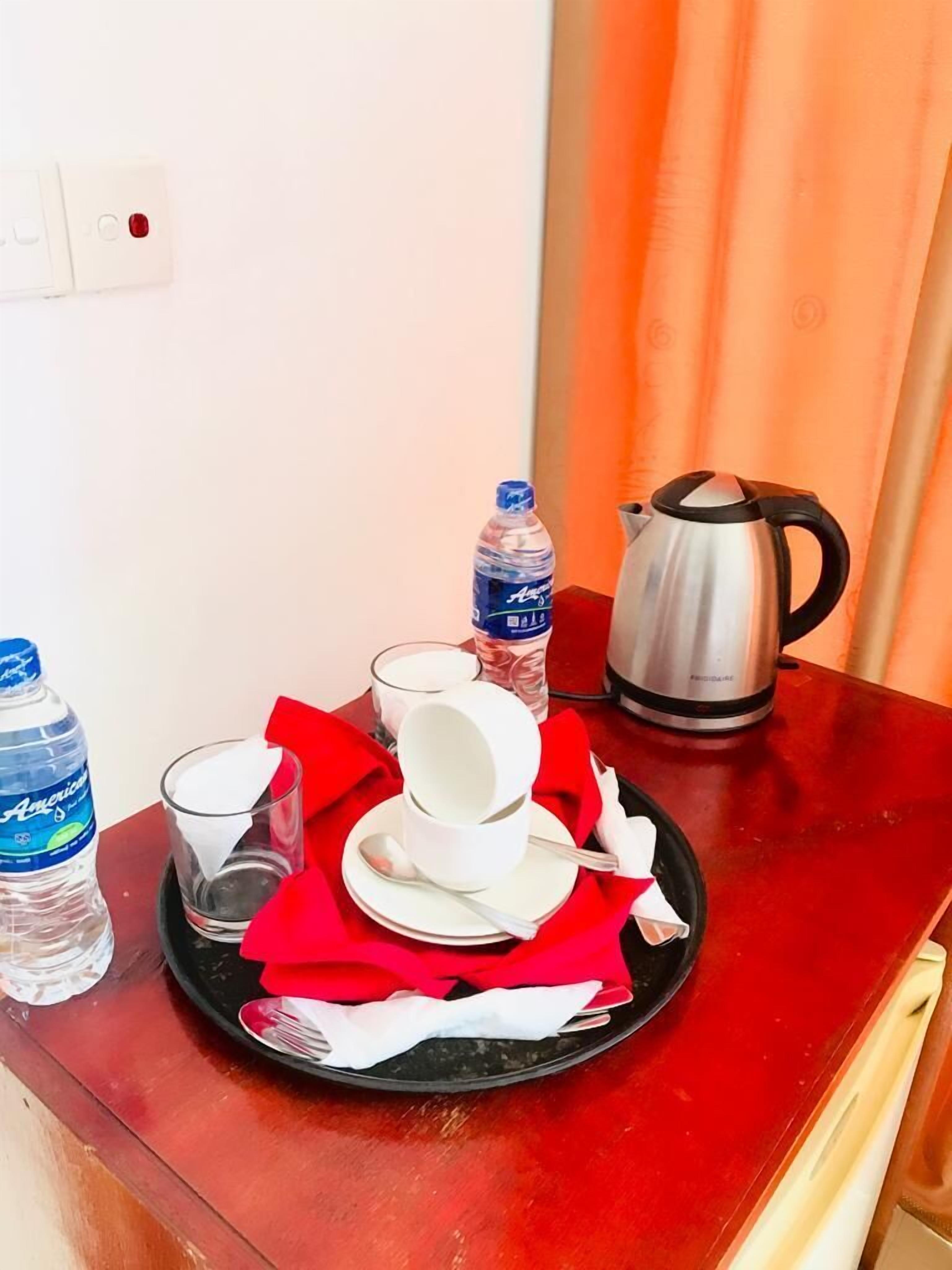 A dining setup with a plate of white dishes, a red napkin, a water bottle, a glass, and a kettle on a wooden table.