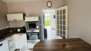 Cocina compacta con armarios blancos, microondas, horno y comedor con mesa de madera y dos sillas.