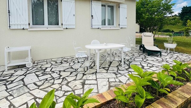 Una casa con tejado de baldosas, un patio con suelo de mosaico y un borde de ladrillo con plantas.