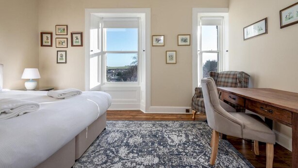 A hotel room with a bed, a desk, a chair, a lamp, and a view through the door.