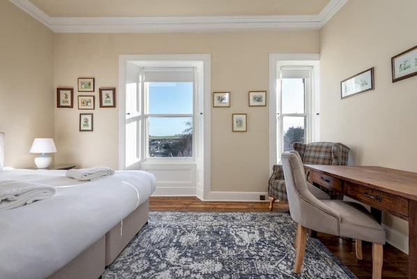 Une chambre d’hôtel avec un lit, un bureau, une chaise, une lampe et des tableaux encadrés aux murs.