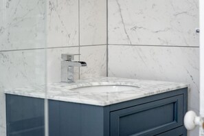A bathroom with a marble sink, a modern faucet, and a blue cabinet.