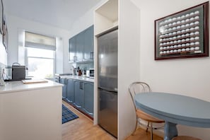 Une cuisine moderne avec des meubles gris, un réfrigérateur en acier inoxydable et un coin repas comprenant une table et des chaises bleues.