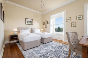 A bedroom with two beds, a sitting area with a chair, a chandelier, and framed pictures on the walls.
