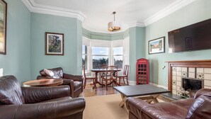 A living room with leather sofas, a round coffee table, a dining table with chairs, a fireplace, and a television.