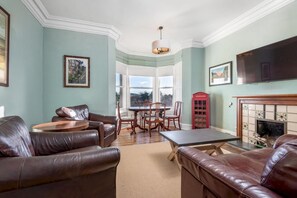 Un salon avec des canapés en cuir, une table basse ronde, une table à manger avec des chaises, une cheminée et un téléviseur.