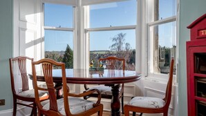 A dining area with a round table and four chairs, large windows with a view of the outdoors, and a red cabinet.