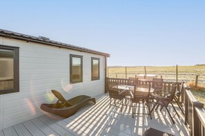 A covered outdoor area with a table and chairs, a wicker chair, and a view of a field.