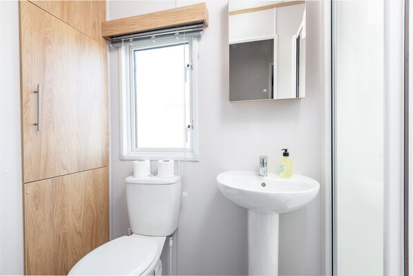 Un baño moderno con un mueble de madera, inodoro, ventana, lavabo y espejo.