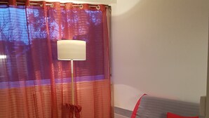 A room with a wooden floor, a white sofa with red and black cushions, a small white table, and a floor lamp.
