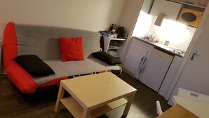 A compact living space with a sofa, a small table, and a kitchenette area.