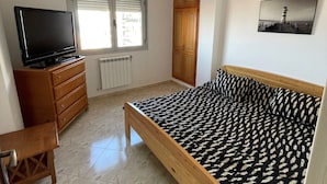 Une chambre à coucher avec un lit, une commode, une télévision et une fenêtre avec des stores.