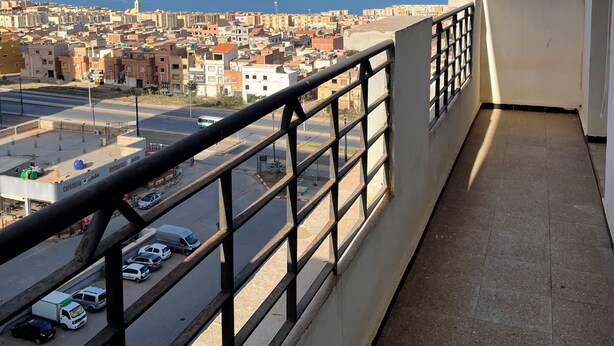 Un balcon doté d’une balustrade en métal, offrant une vue sur le paysage urbain et la mer.