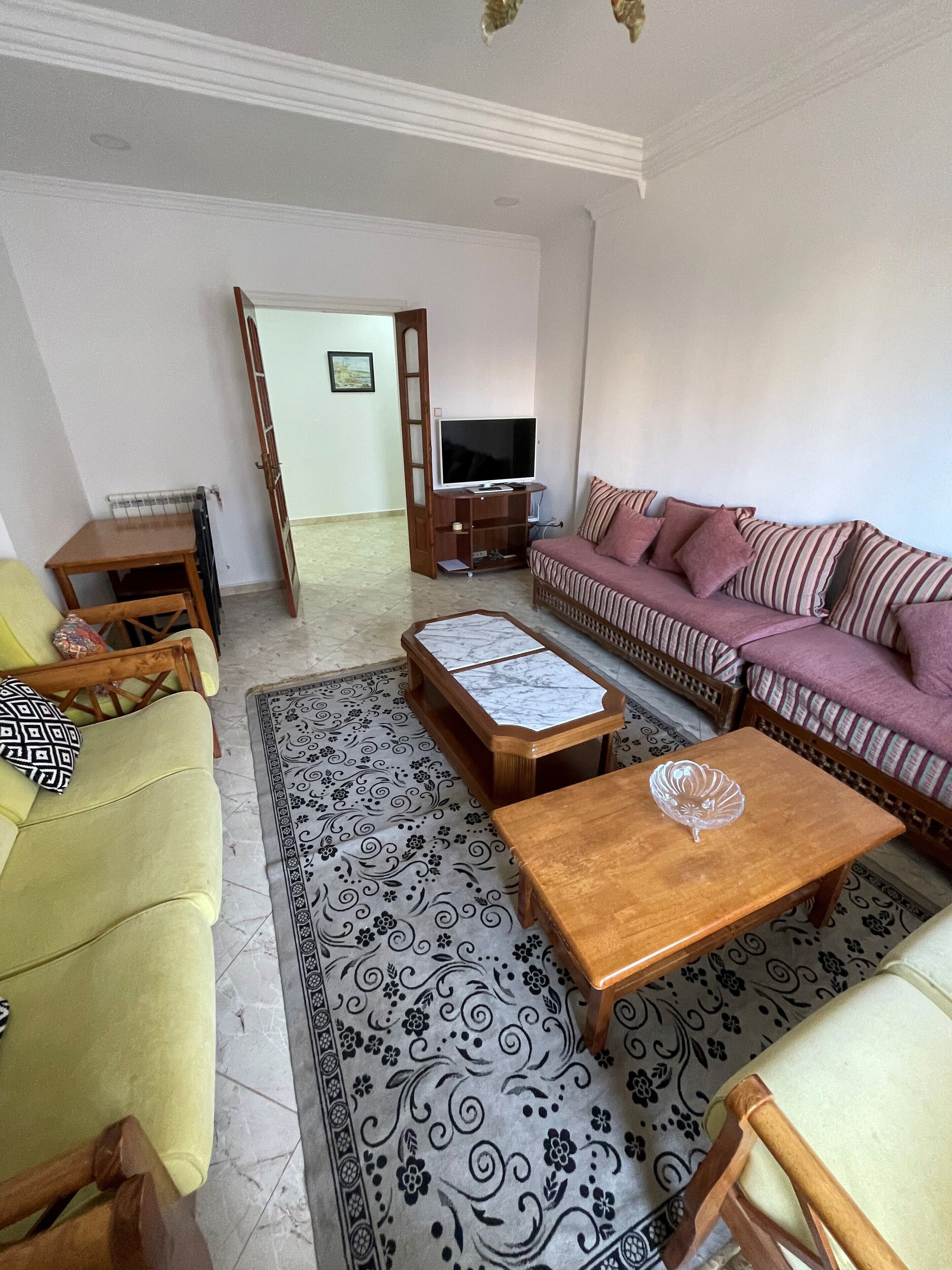 Un salon comprenant un canapé, une table basse, un meuble pour la télévision et un tapis à motifs.