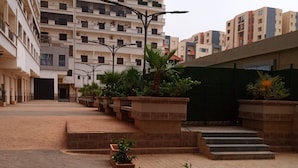 Une cour intérieure agrémentée de plantes en pot, un escalier et, au fond, un immeuble de grande hauteur.