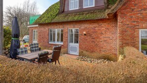 A brick house with a sloped roof covered in moss, a patio with a table and chairs, and a green structure in the background. - 1 bedroom stunning apartment in Neukirchen (Neukirchen)