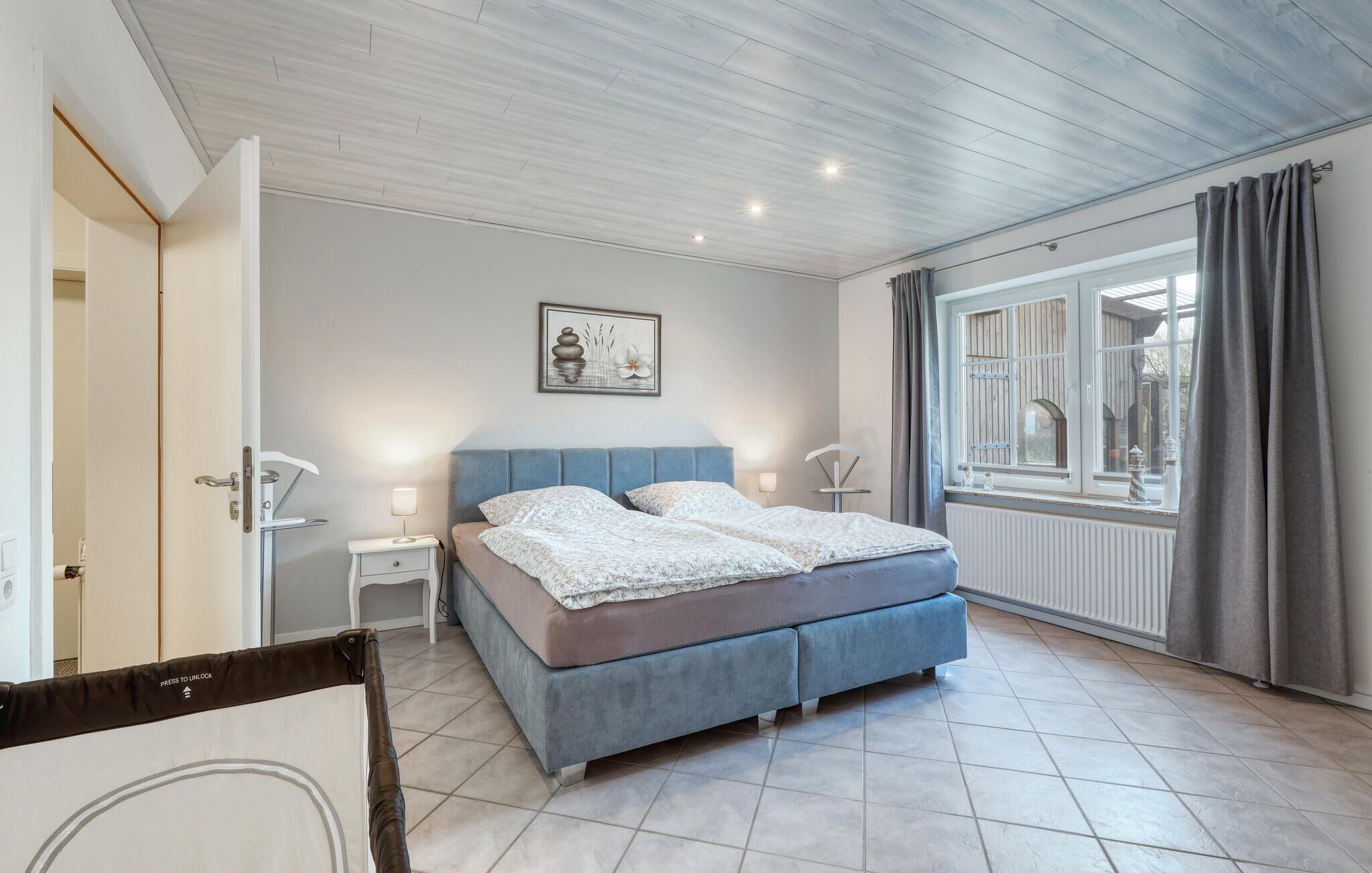 Un dormitorio con cama, mesitas de noche, ventana con cortinas e iluminación empotrada en el techo.
