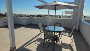 A rooftop terrace with a glass table and chairs, a large umbrella, and a clear view of the city skyline.