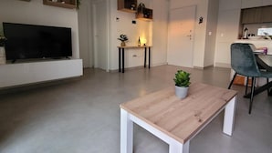 A modern living room with a flat-screen TV, a wooden coffee table, and a grey chair.