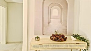 Um interior moderno com design minimalista, apresentando uma mesa consola clara com base trançada, uma pequena planta em vaso e uma composição decorativa de pinhas e folhagem.
