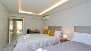 Quarto de hotel moderno com uma cama grande, uma mesa de cabeceira com abajur e uma pequena escrivaninha com uma planta.