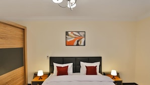 A hotel room with a large bed, two bedside tables with lamps, a modern headboard, a wooden accent wall, and a framed abstract painting. - Parkside boutique 3 bedroom apartment (Cairo)