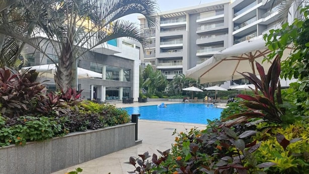 A modern hotel with a swimming pool surrounded by lush greenery and palm trees. - Parkside boutique 3 bedroom apartment (Cairo)