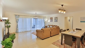 A spacious living room with a sofa set, a dining table with chairs, and a large window with curtains. - Parkside boutique 3 bedroom apartment (Cairo)