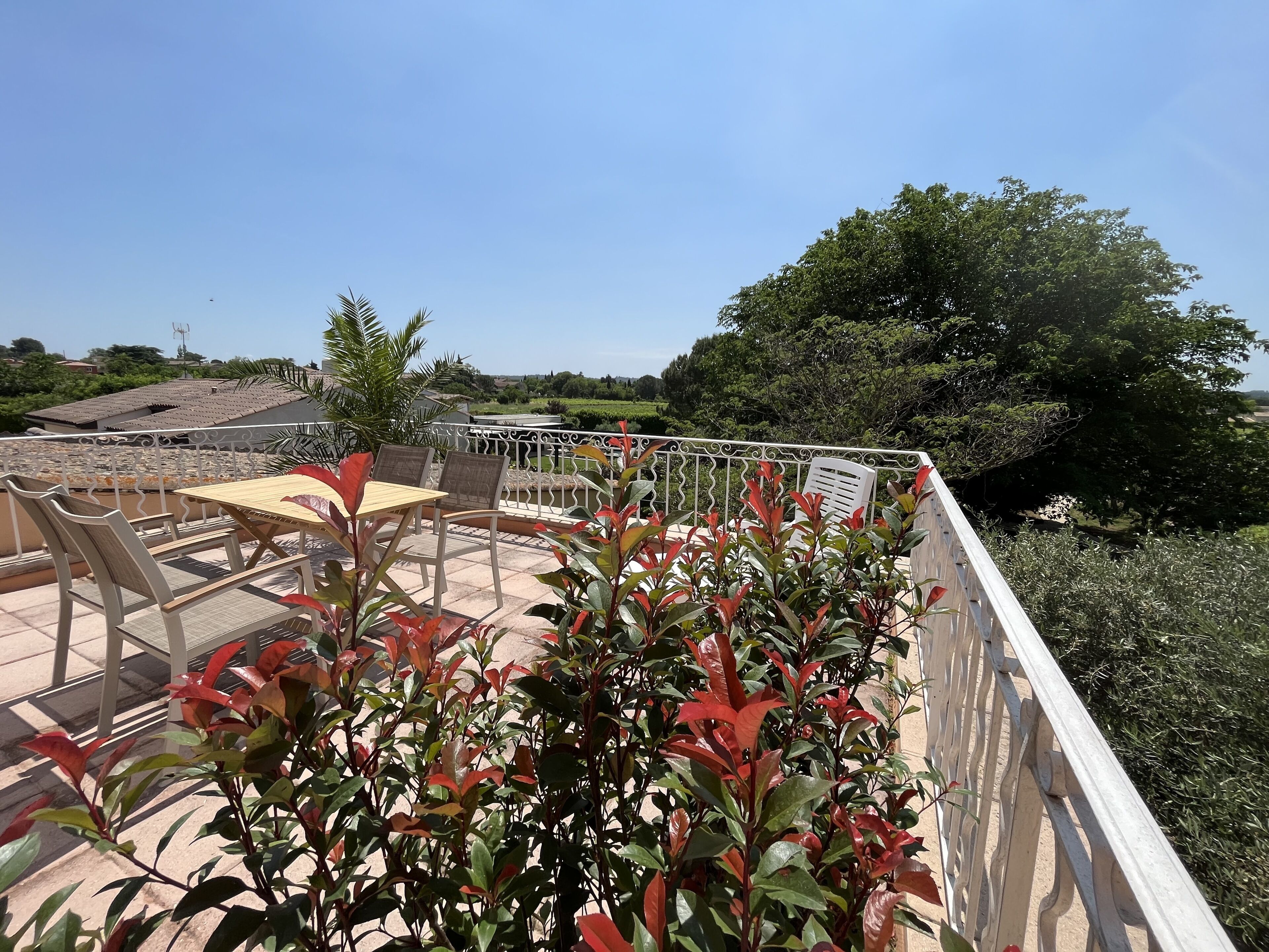 Eine Terrasse mit Tisch und Stühlen, umgeben von Pflanzen und Blick auf die Landschaft.