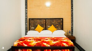 Una cama con colcha estampada, dos almohadas y una mesita de noche con una botella y un vaso.