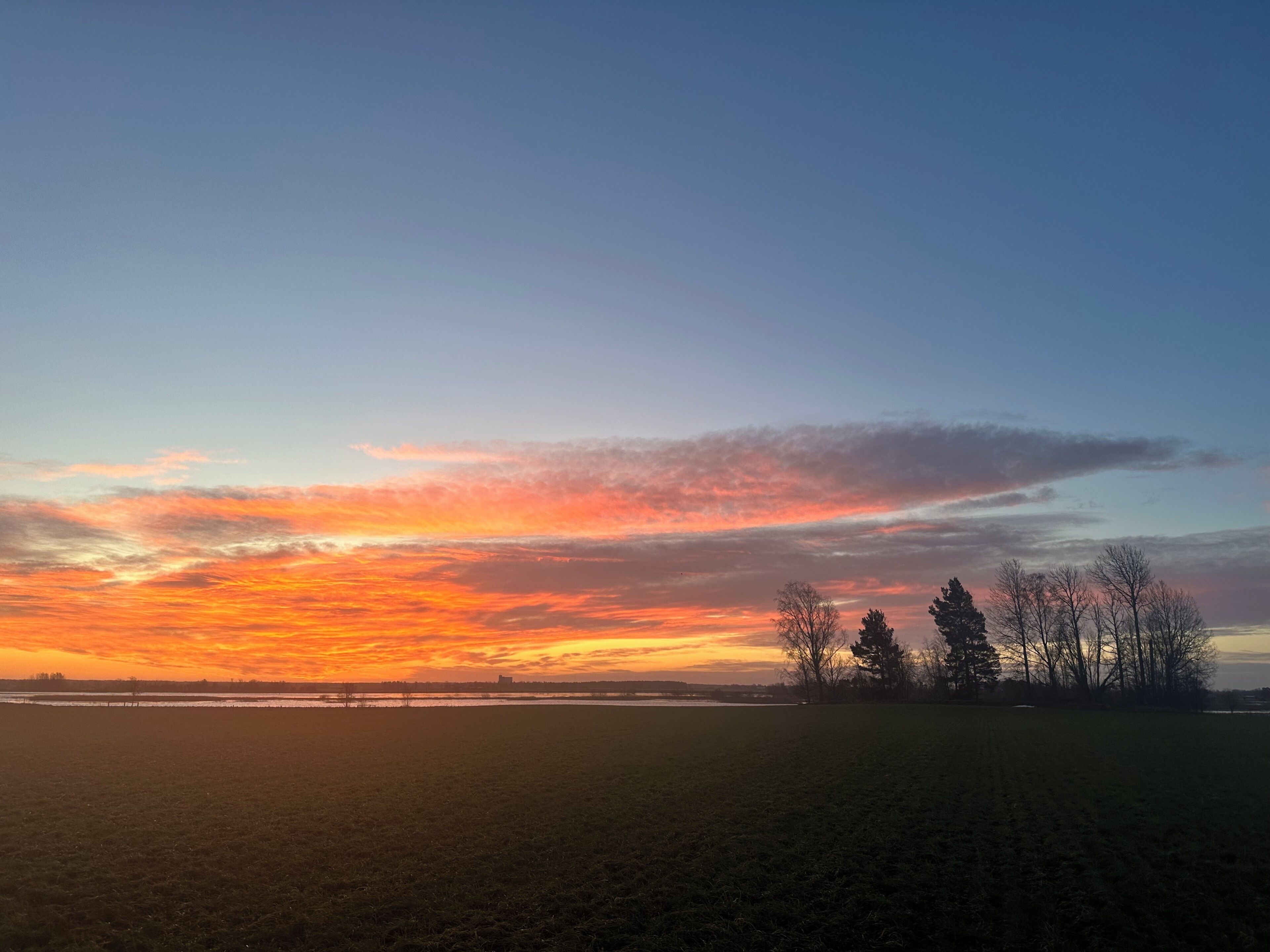 Laaja, avoin pelto ja auringonlaskun värittämä taivas.