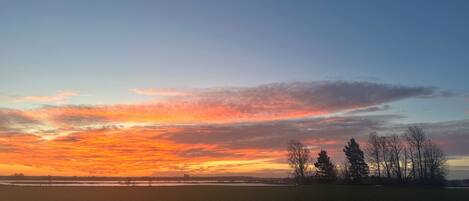 Laaja, avoin pelto ja auringonlaskun värittämä taivas.