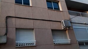 Un edificio de varios pisos con fachada plana, unidades de aire acondicionado y ventanas con persianas.