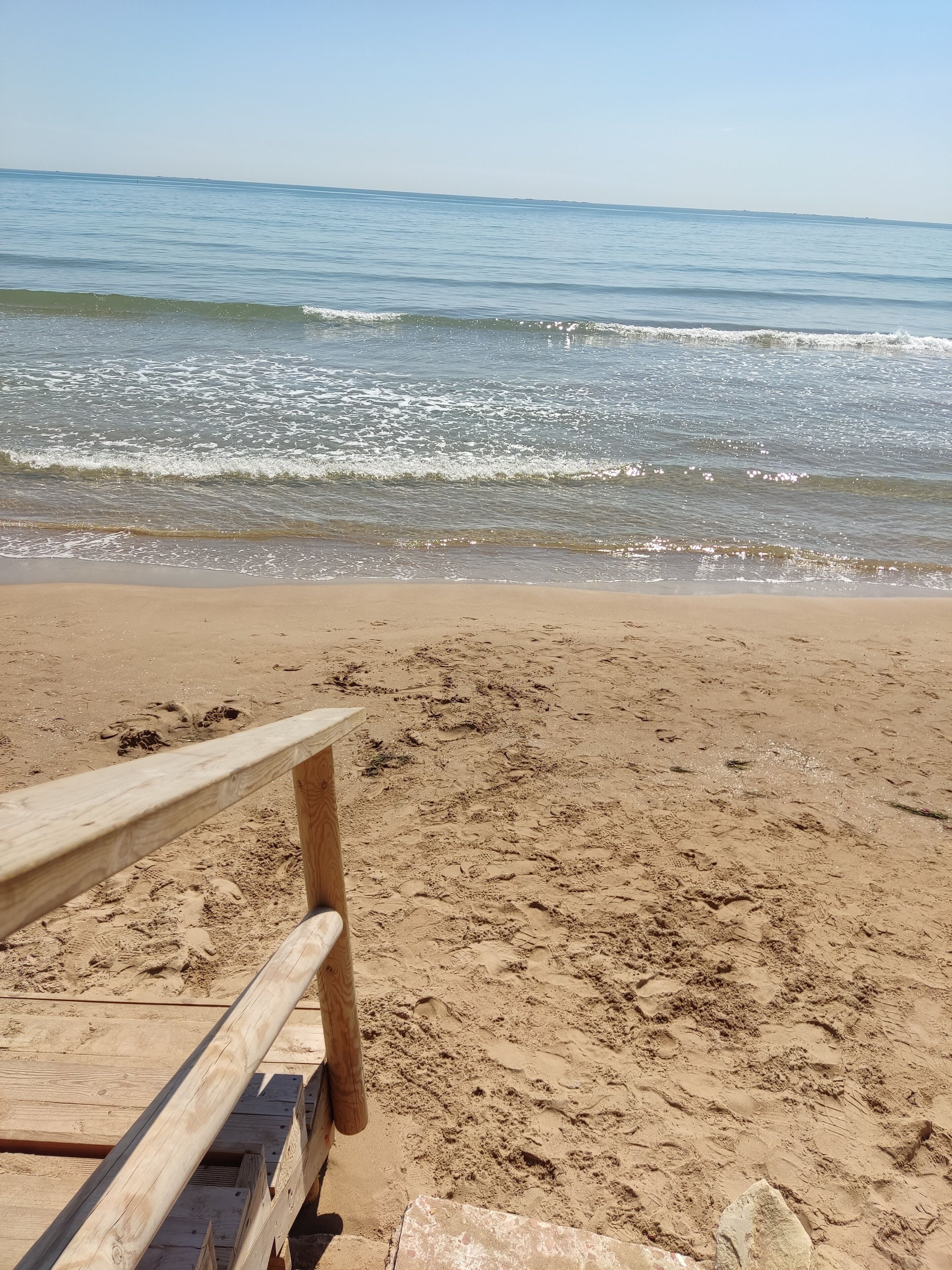 En strandstol av trä på en sandstrand med havsvågor i bakgrunden.