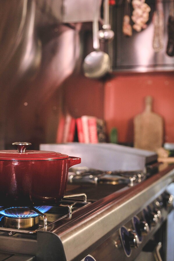 A kitchen with a red pot on a stove, a wooden cutting board, and a hanging pot rack.