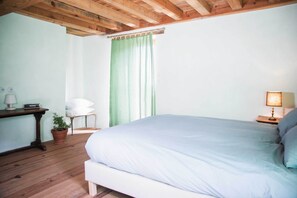 A bedroom with a bed, a chair, a table, a lamp, and a potted plant. - Chambre Avec vue mer Dans L'éco-lodge de Carbonaccio (Chiatra)