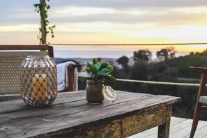 A rustic wooden table with a candle holder and a small potted plant on a balcony overlooking a scenic landscape.