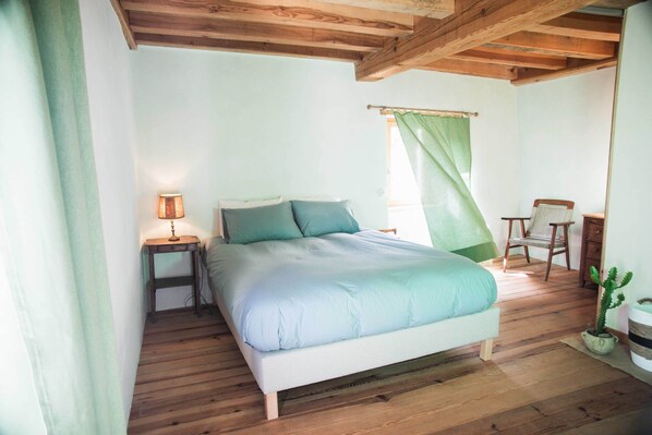 A bedroom with a bed, a nightstand, a chair, and a potted plant. - Chambre Avec vue mer Dans L'éco-lodge de Carbonaccio (Chiatra)
