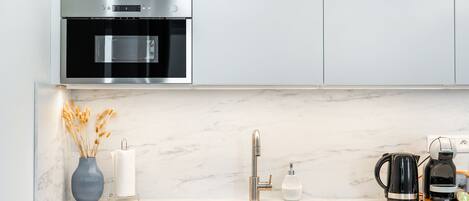 A modern kitchen with a built-in oven, a stainless steel sink, and a coffee maker.
