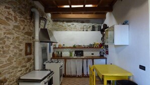 Une cuisine de taille réduite, équipée d’une cuisinière, d’un four et d’un petit réfrigérateur. On y trouve une table et des chaises jaunes, et une poubelle est visible.