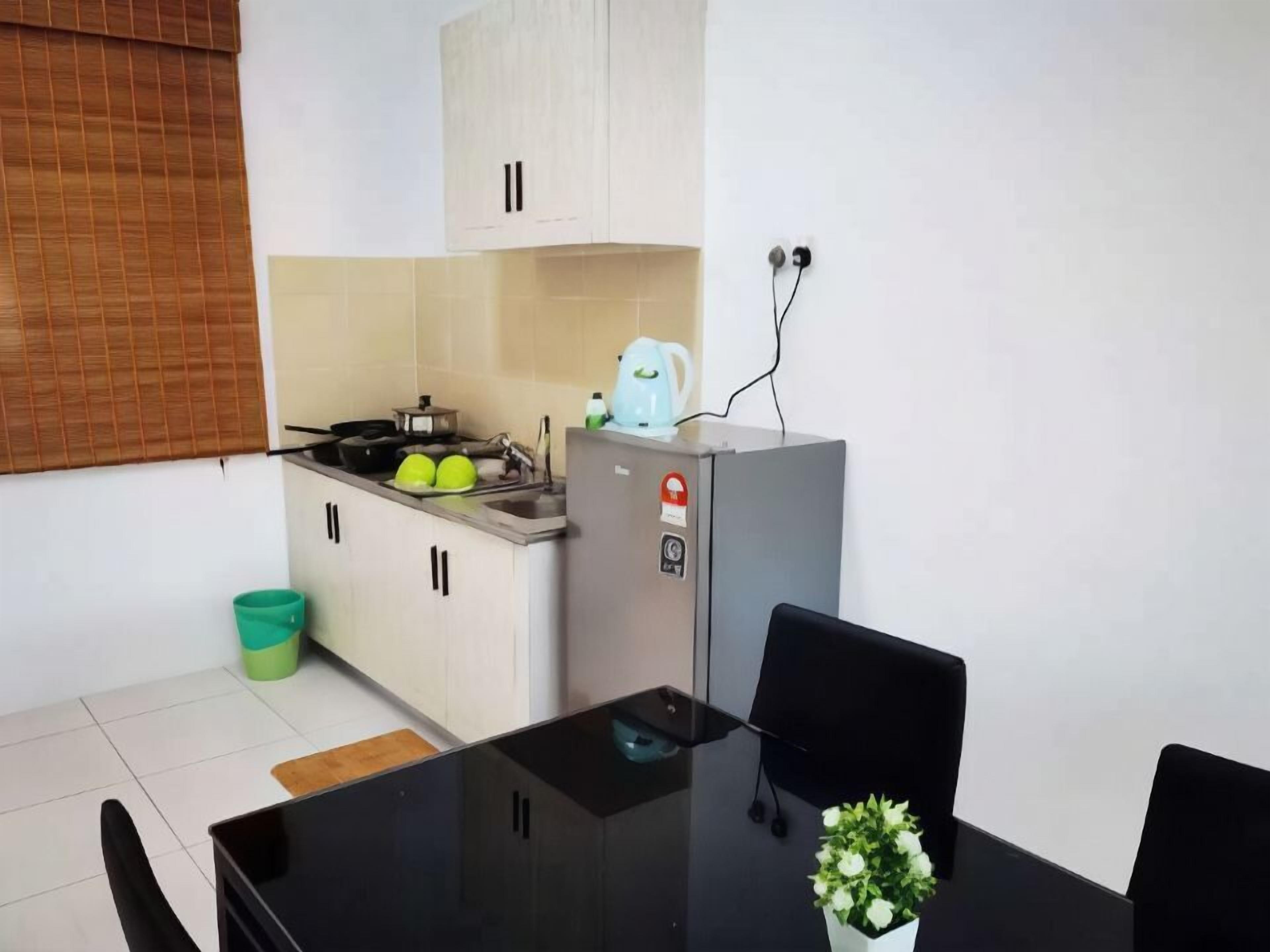 A compact kitchen with a stove, sink, and a small refrigerator. There is a dining table with chairs and a potted plant.