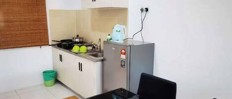 A compact kitchen with a stove, sink, and a small refrigerator. There is a dining table with chairs and a potted plant.