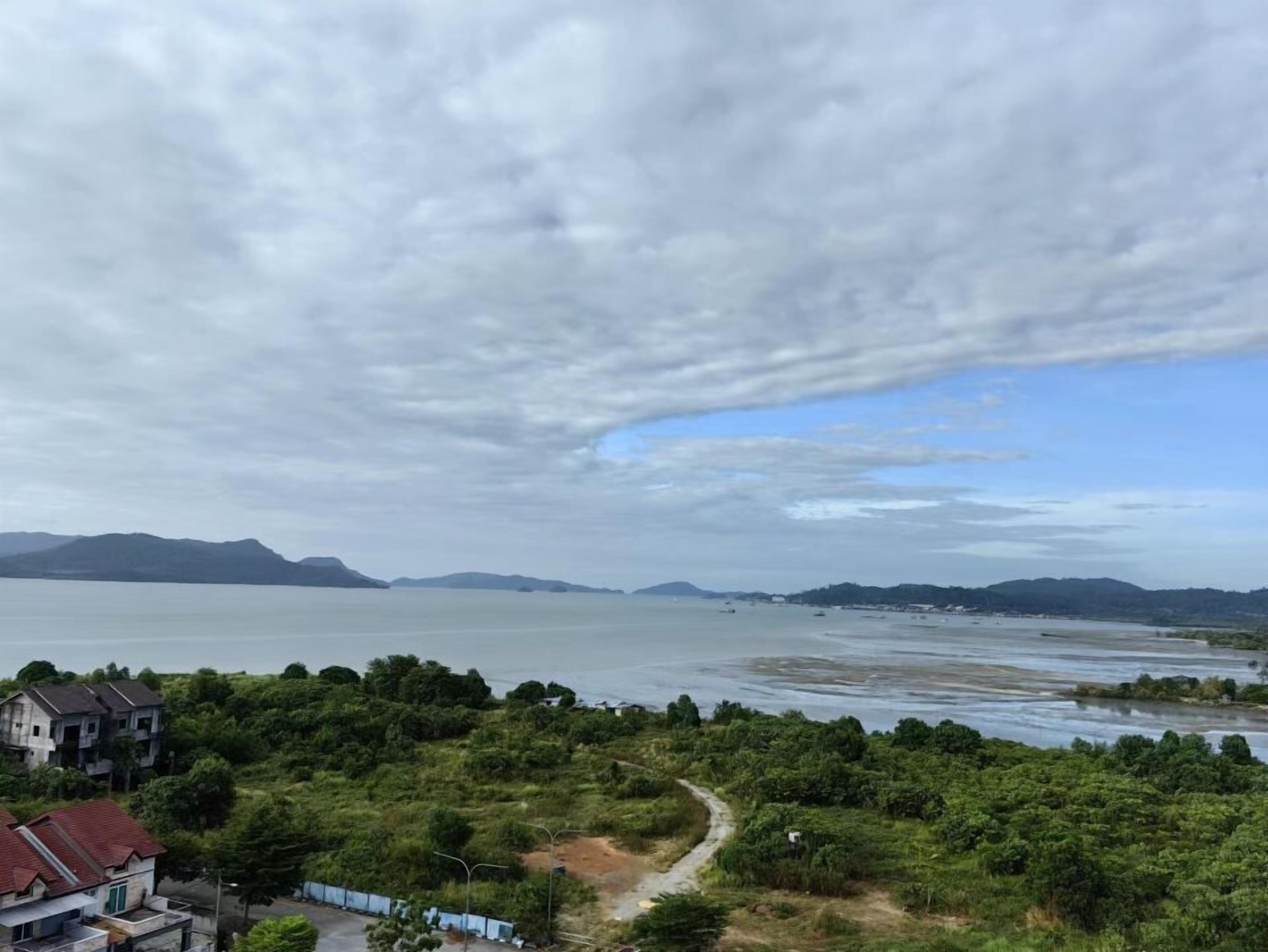 Un paisaje costero con vista al mar, un sendero entre la vegetación y montañas a la distancia.