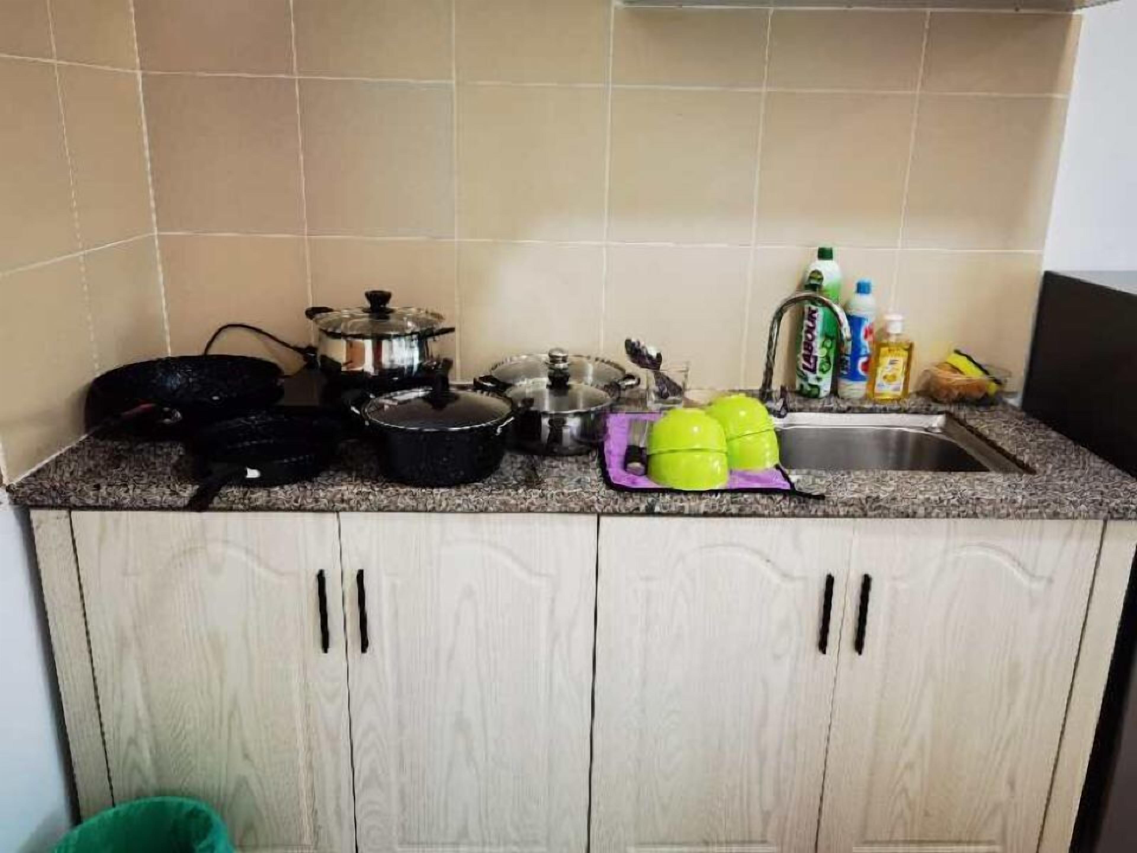 A kitchen with a granite countertop, various pots and pans, a sink, and some cleaning supplies.
