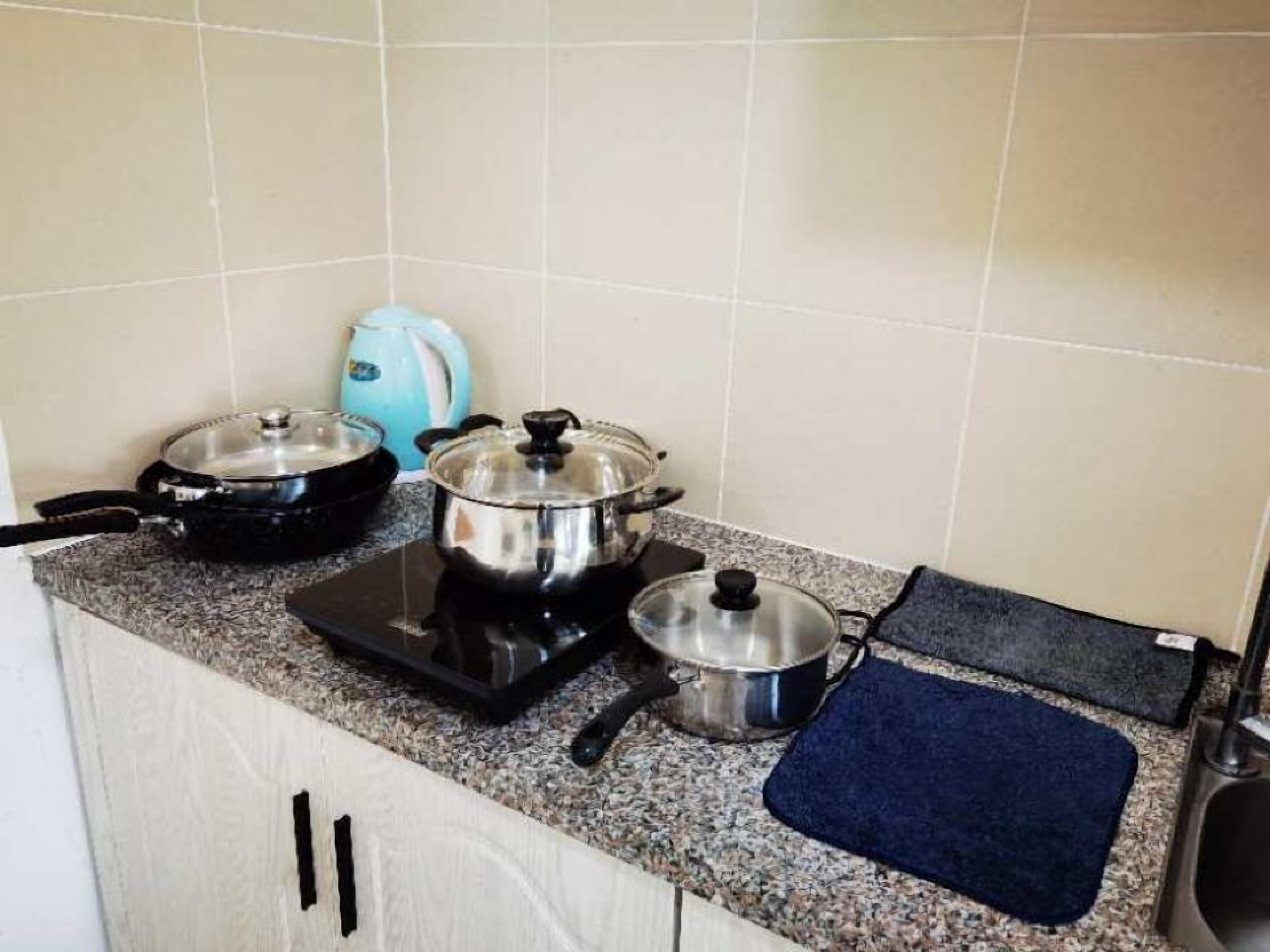 A kitchen with a stove, two pots, a kettle, and a blue mat.