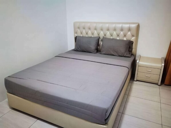 Una cama con cabecera capitonada, dos almohadas y una mesita de noche con cajones.