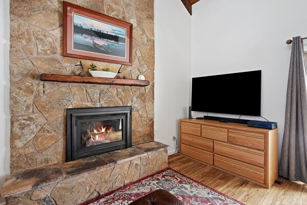 A stone fireplace with a TV above it, wooden cabinets, and a rug.