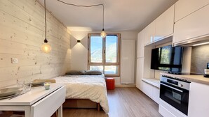 A modern kitchen with a bed, wooden flooring, and a TV. - Superbe Studio Refait à Neuf en Plein Centre Ville Avec Parking (Chamonix-Mont-Blanc)