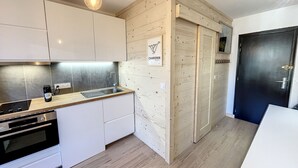 A modern kitchen with white cabinets, a wooden countertop, a built-in oven, and a black door. - Superbe Studio Refait à Neuf en Plein Centre Ville Avec Parking (Chamonix-Mont-Blanc)