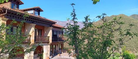 A two-story house with a balcony, a stone pathway, and a view of mountains.